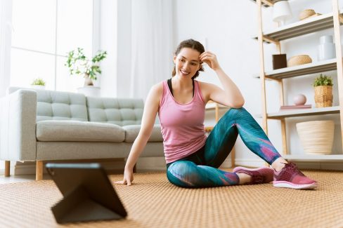 Young woman in activewear watching online courses on tablet while exercising at home.